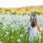 a girl in a white dress in a field of dandelions