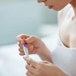 a woman looks at a pregnancy test stick in her hand