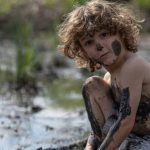 a young boy is covered in mud and dirt in a swamp at the park e1620999104306