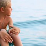 boy sitting on a wooden jetty at sea beach e1619101610526