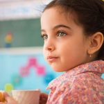 cute little hispanic girl with cup of milk at daycare