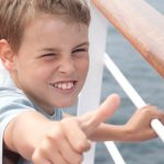 little boy shows ok on deck of big passenger ship e1619763552846