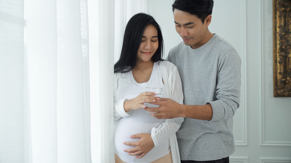 man handing a pregnant woman a glass of water