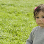 posing serious baby girl sit on grass alone e1618296550671