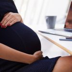 pregnant woman holds stomach at desk