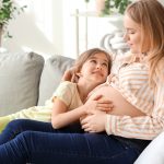 pregnant woman sits on sofa with daughter