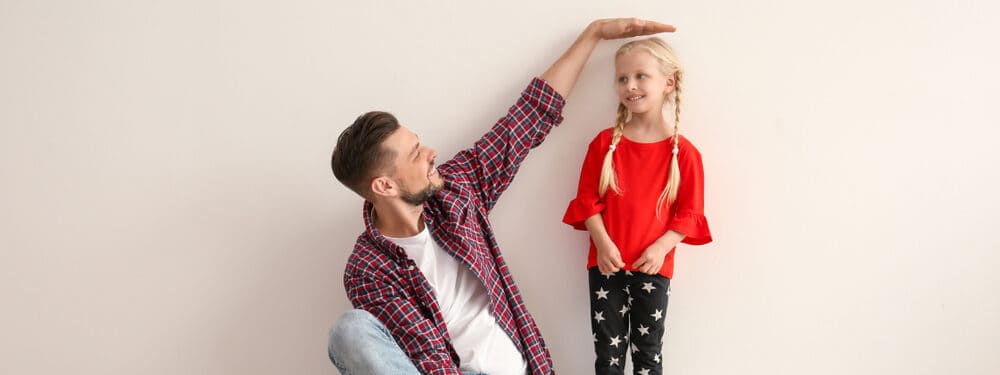 young man measuring little girls height indoors e1619437286335